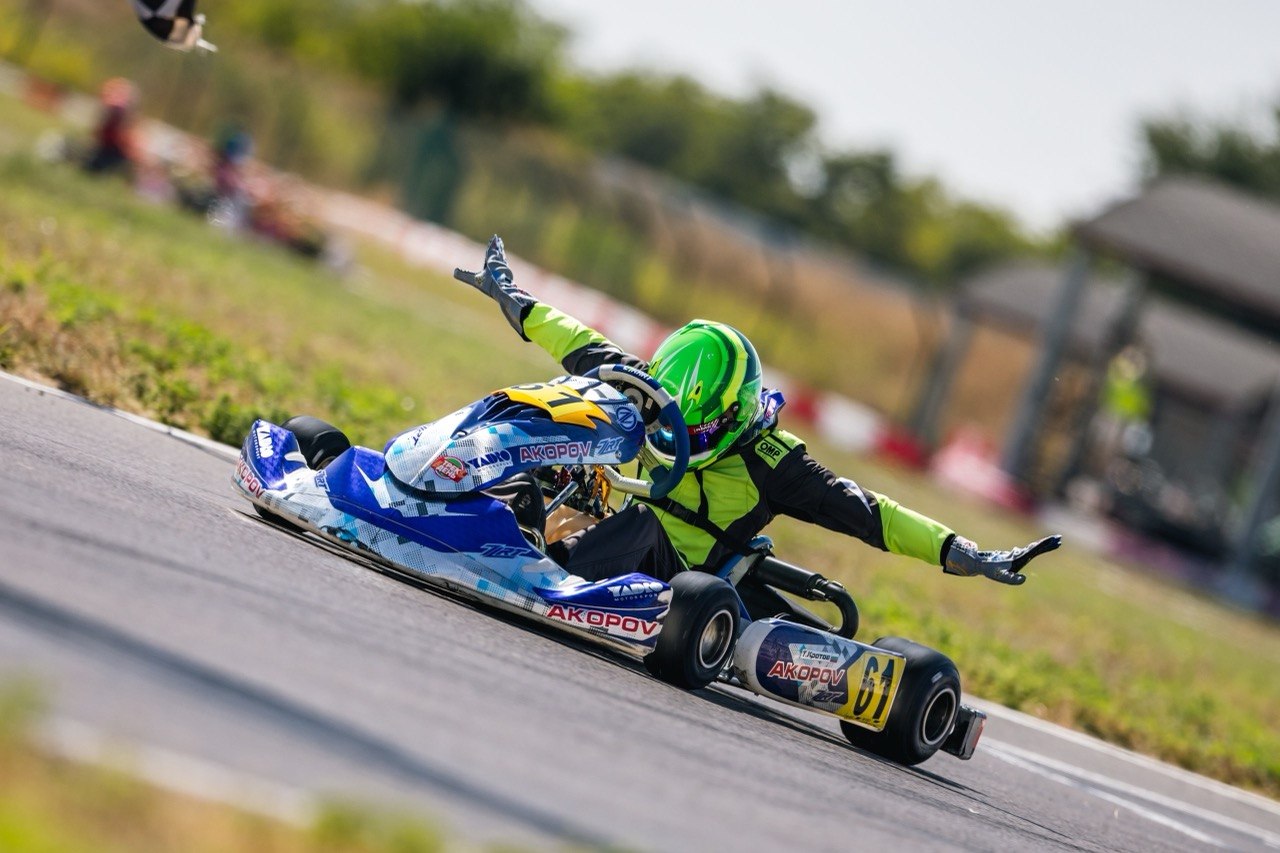 Trofim Krotov celebrating with both arms raised on kart 661 after crossing the finish line.